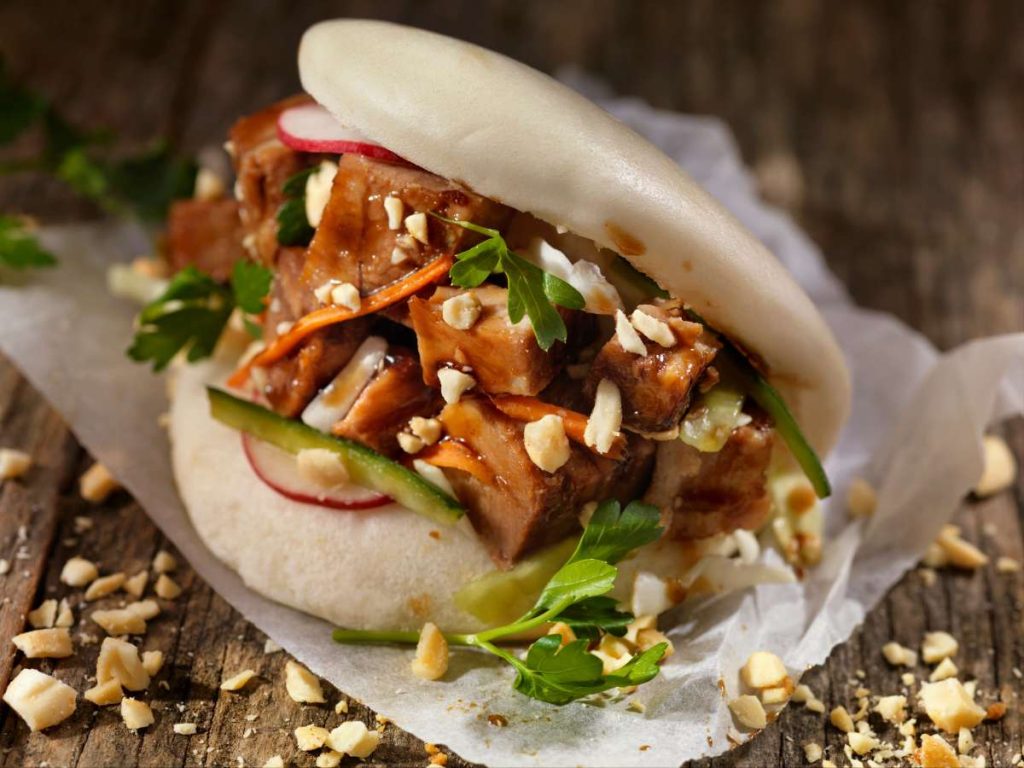 A bao bun filled with various meats and vegetables.