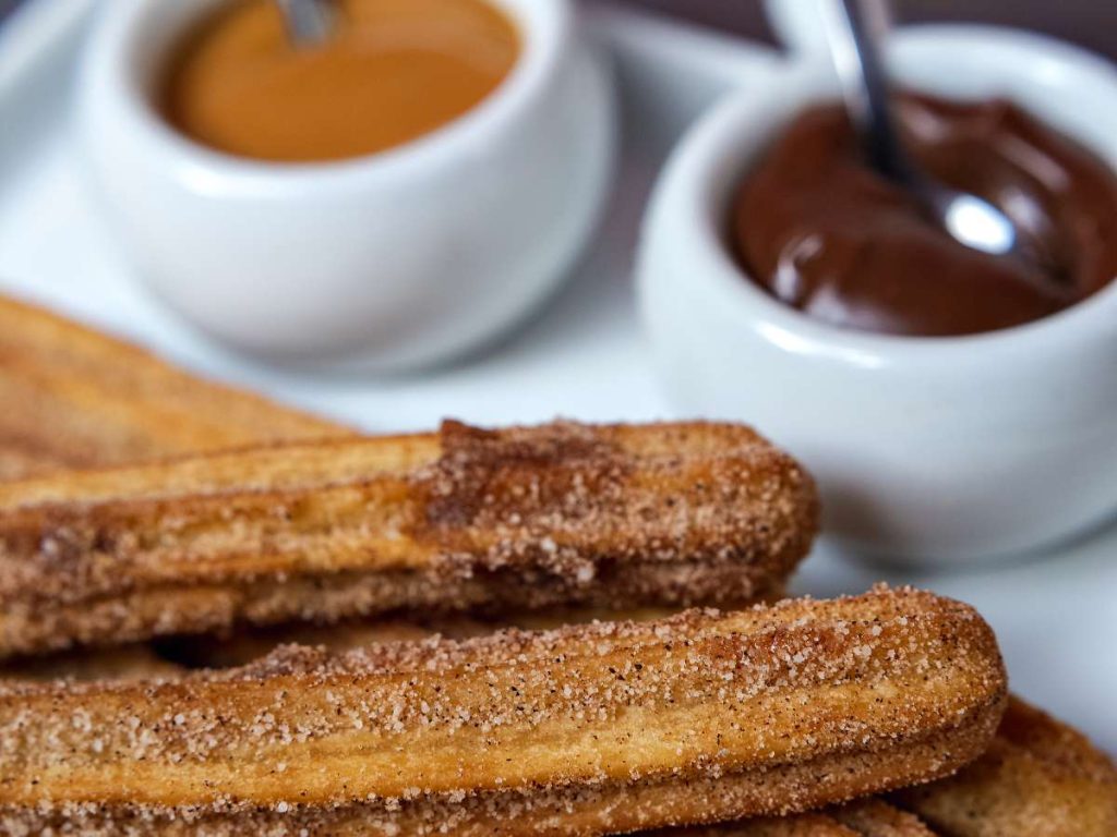 Several fresh churros with various dips nearby.